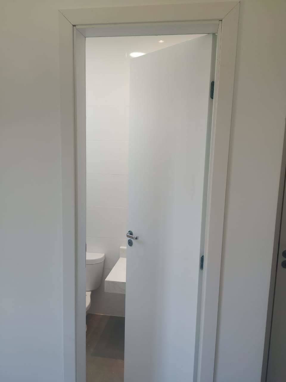 Uma porta branca está aberta para um banheiro com vaso sanitário e pia.