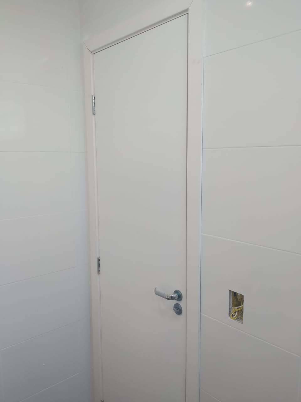 Uma porta branca com uma maçaneta está em um banheiro.