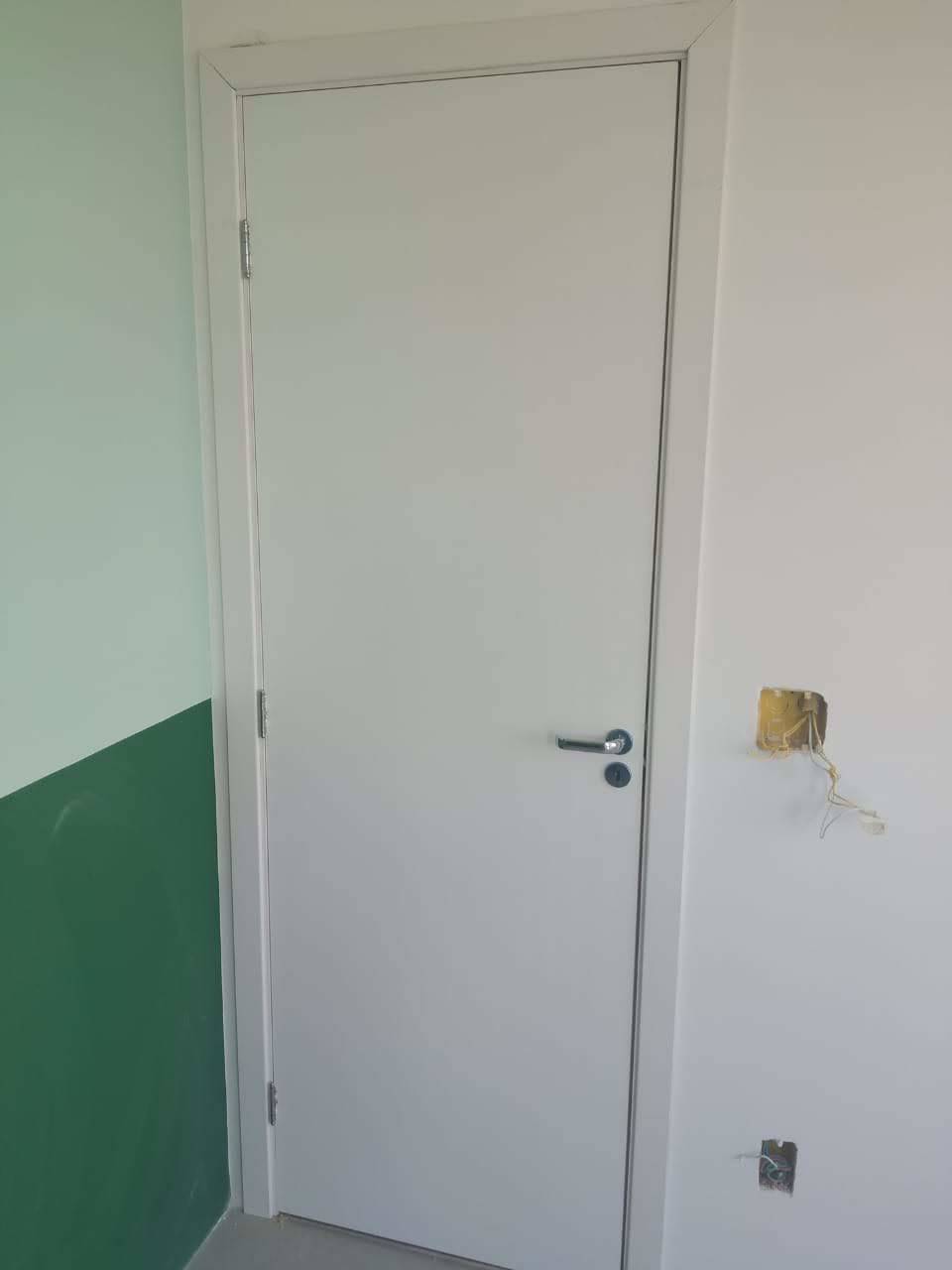 Uma porta branca está em uma sala ao lado de uma parede verde.
