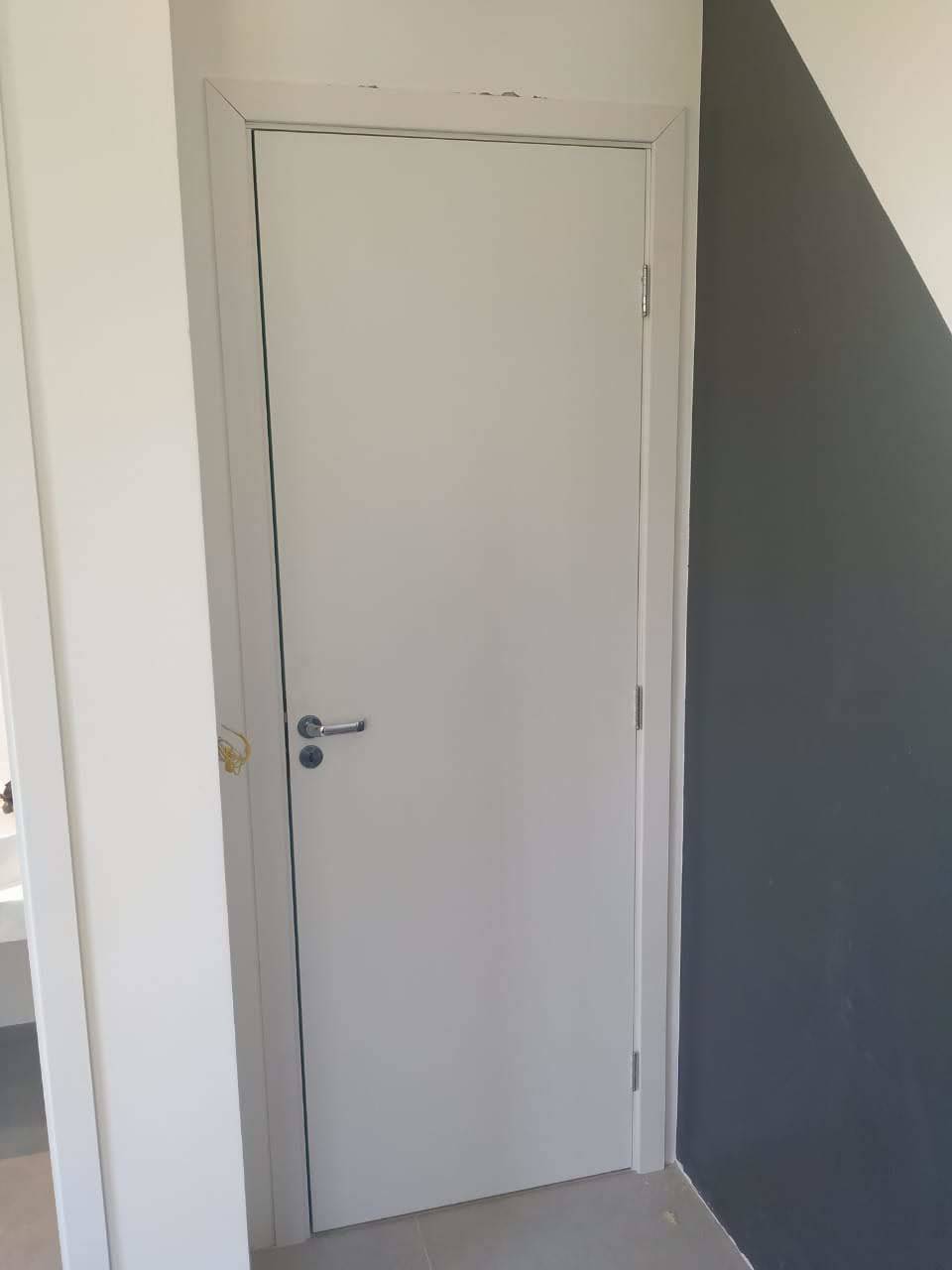 Uma porta branca está em um corredor ao lado de uma parede.