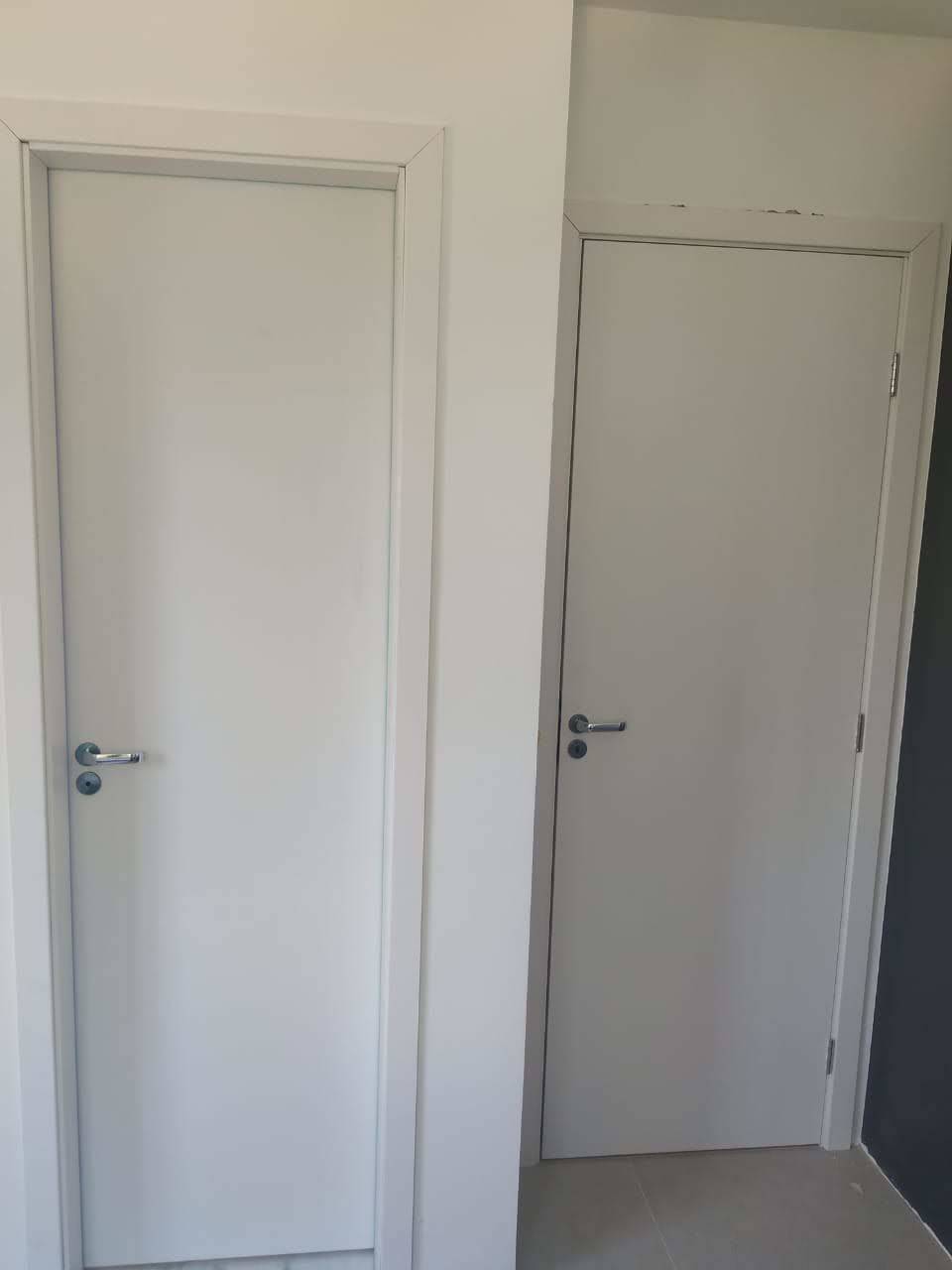 Duas portas brancas estão lado a lado em uma sala.