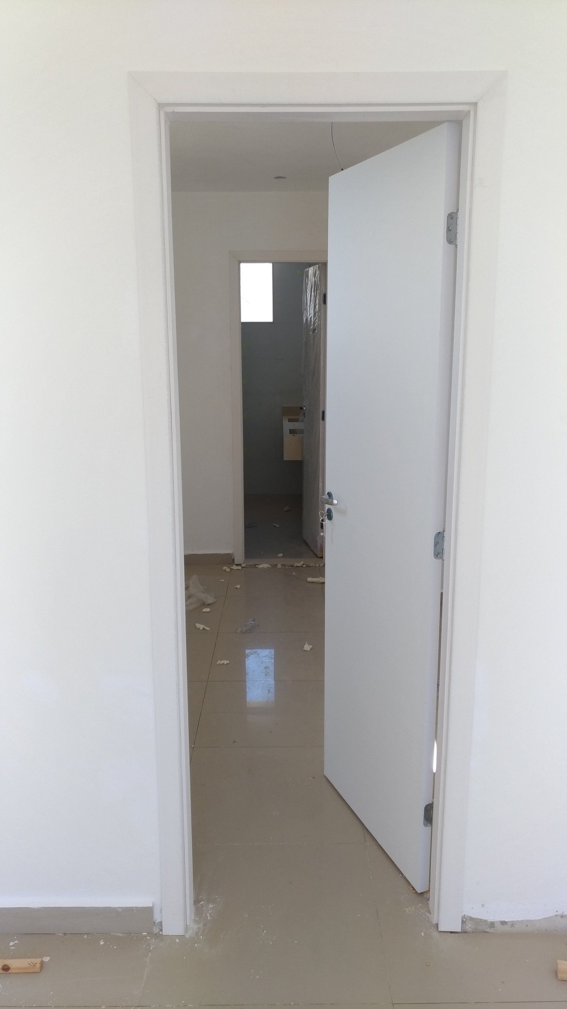 Uma porta branca está aberta em uma sala que leva a um banheiro.