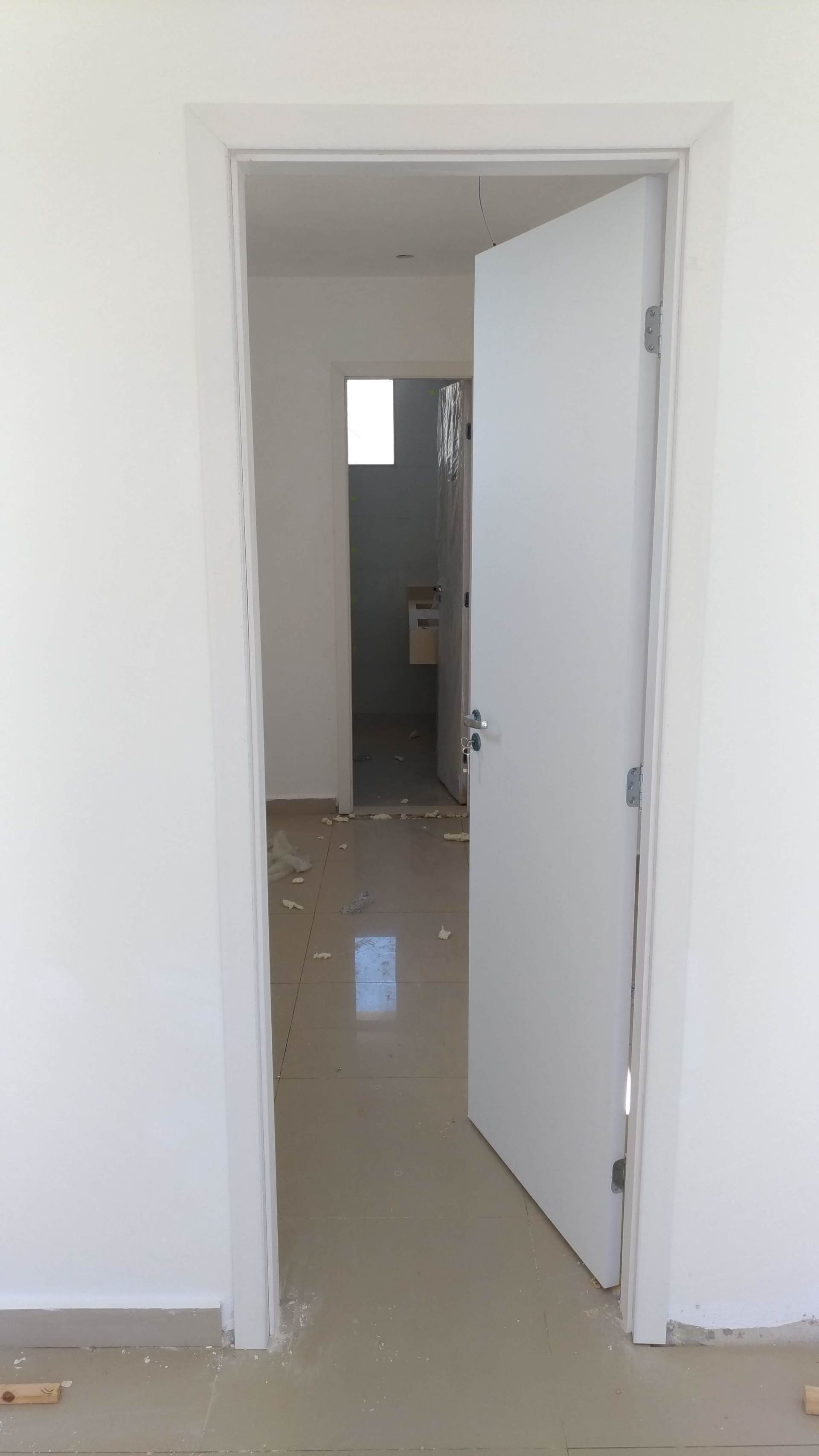 Uma porta branca está aberta em uma sala vazia que leva a um banheiro.