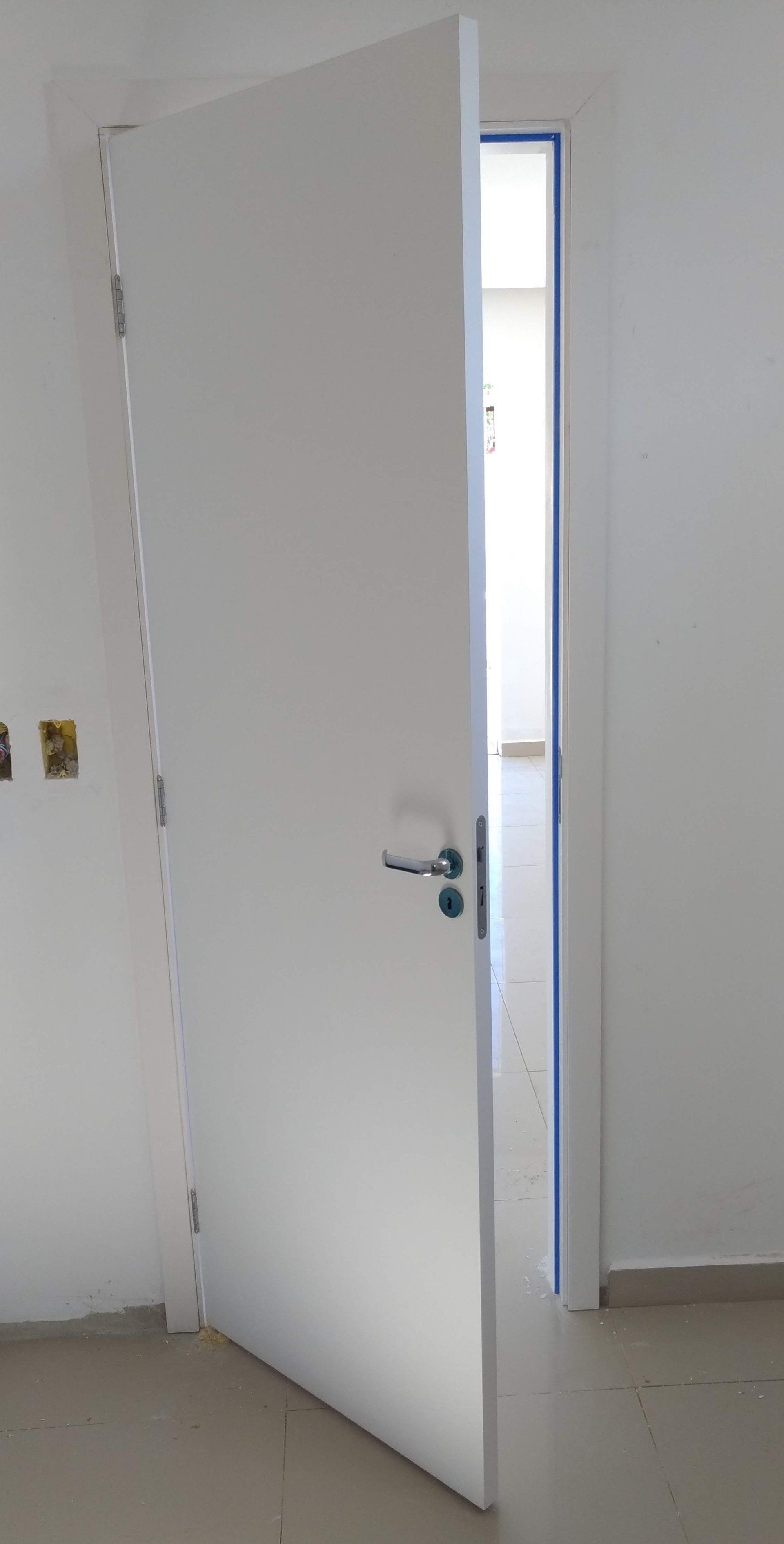 Uma porta branca está aberta em uma sala com uma parede branca.