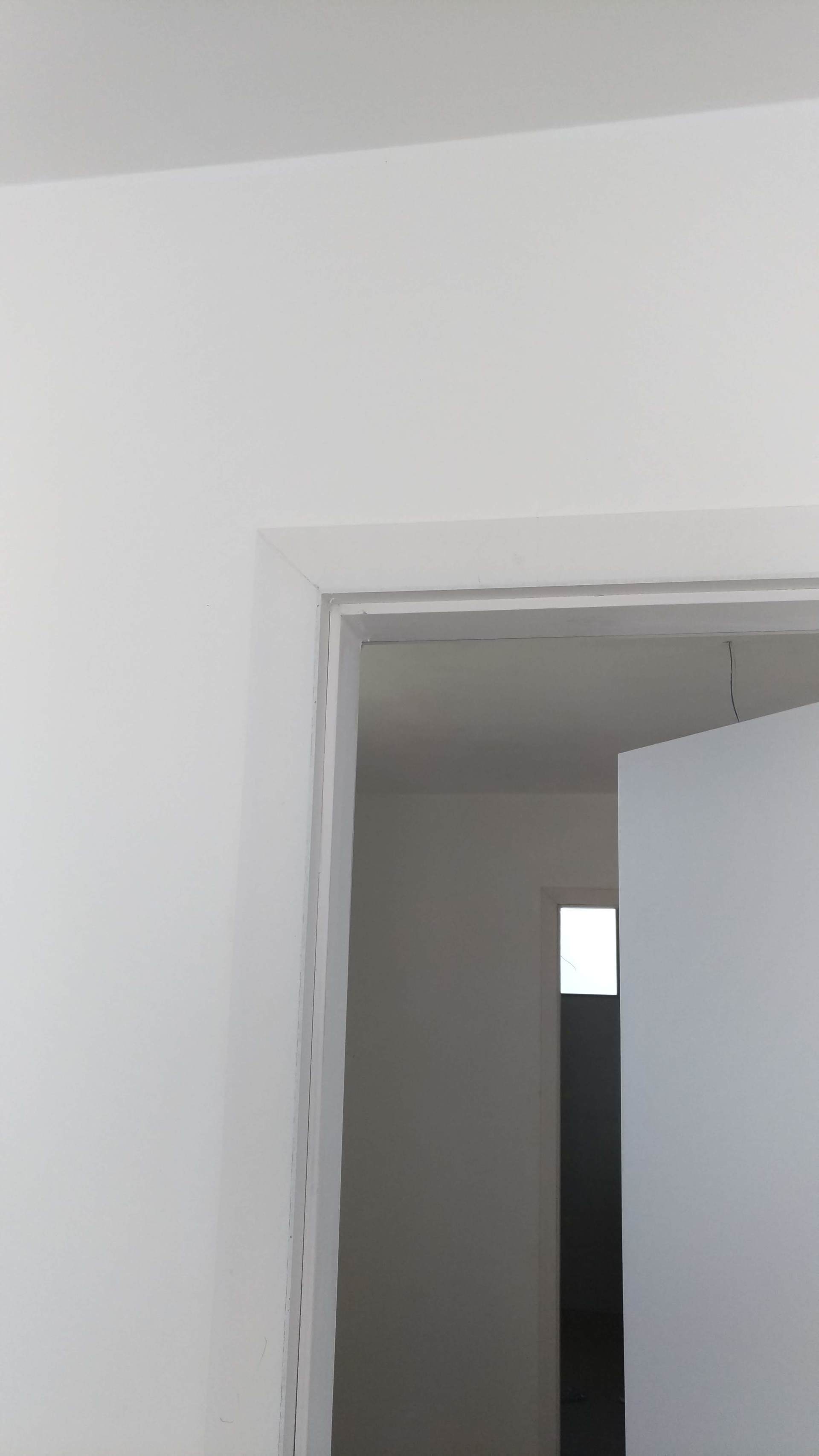 Uma porta branca está aberta em uma sala com uma parede branca.