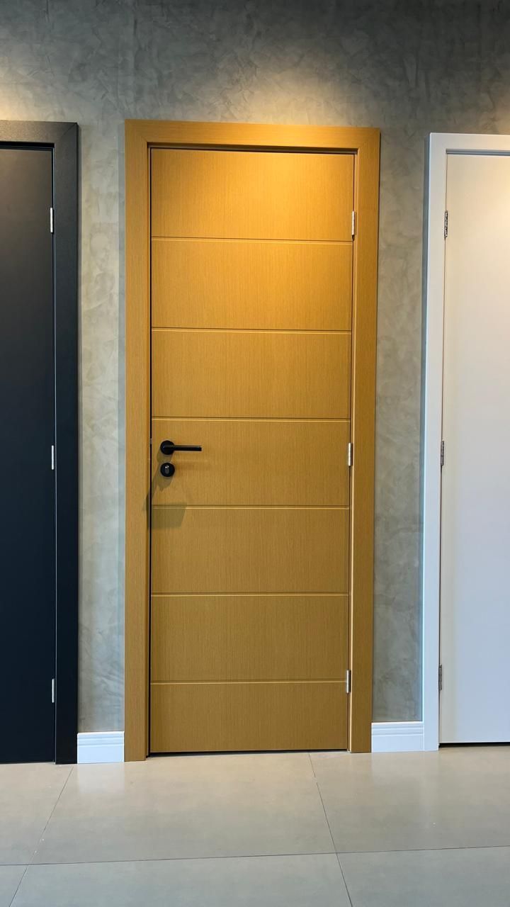 Uma porta de madeira está ao lado de uma porta preta e uma porta branca em uma sala.