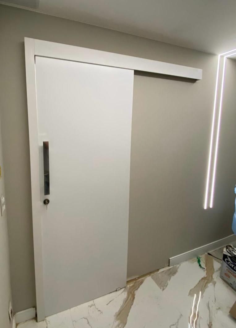Uma porta de correr branca com uma maçaneta preta está em uma sala.