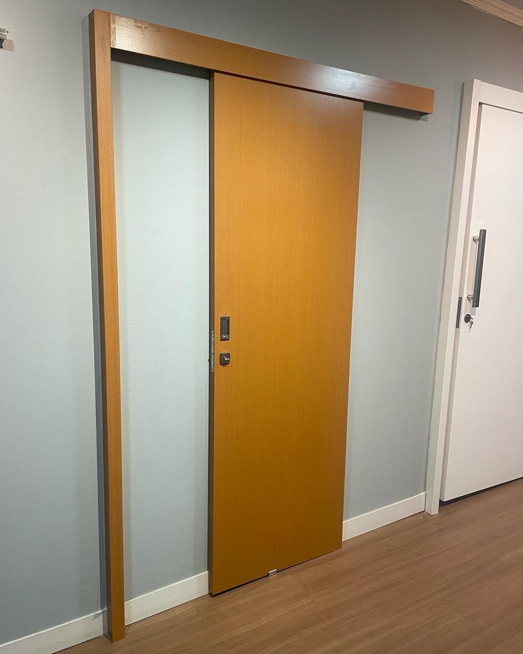 Uma porta de correr de madeira fica em um corredor ao lado de uma porta branca.