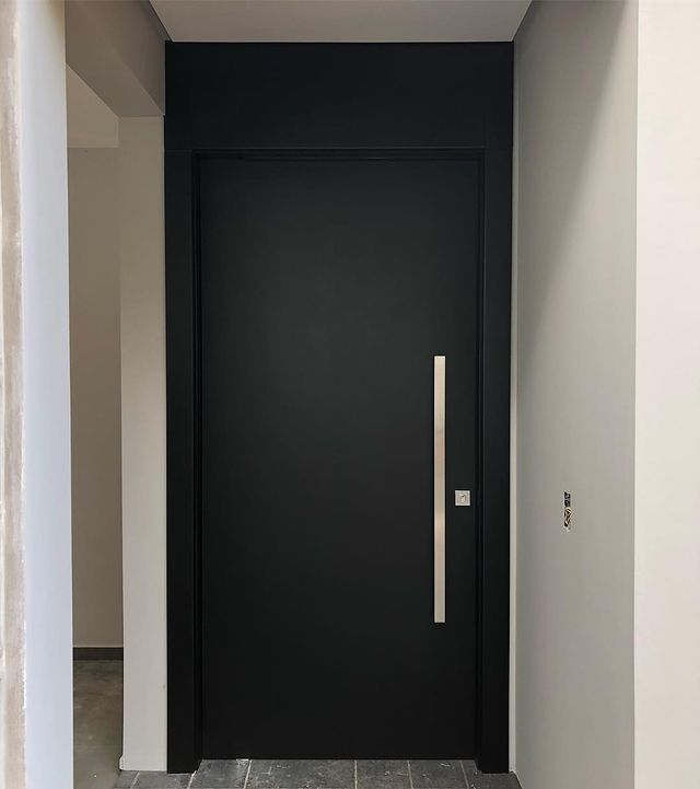 Uma porta preta com uma maçaneta de aço inoxidável está em um corredor.