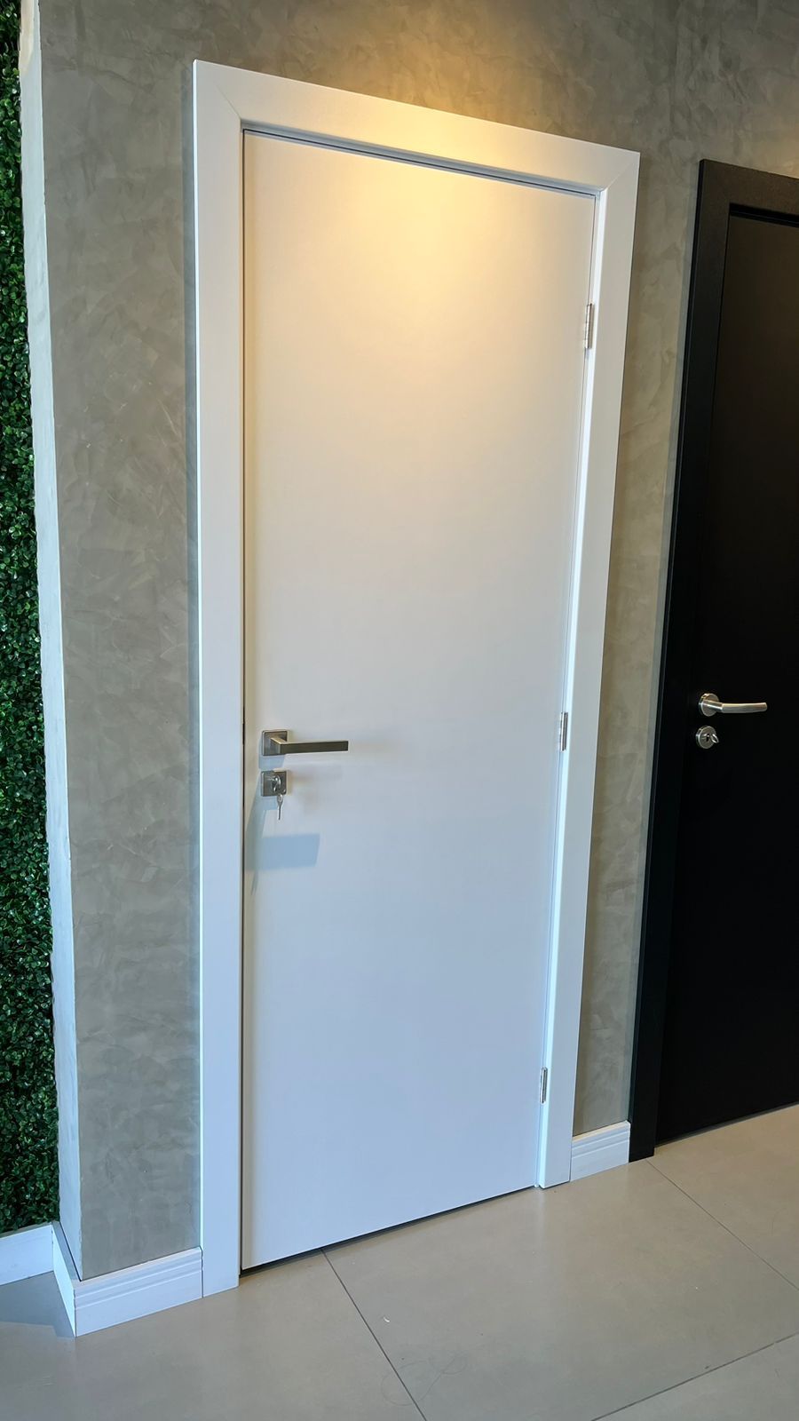 Uma porta branca está ao lado de uma porta preta em um corredor.