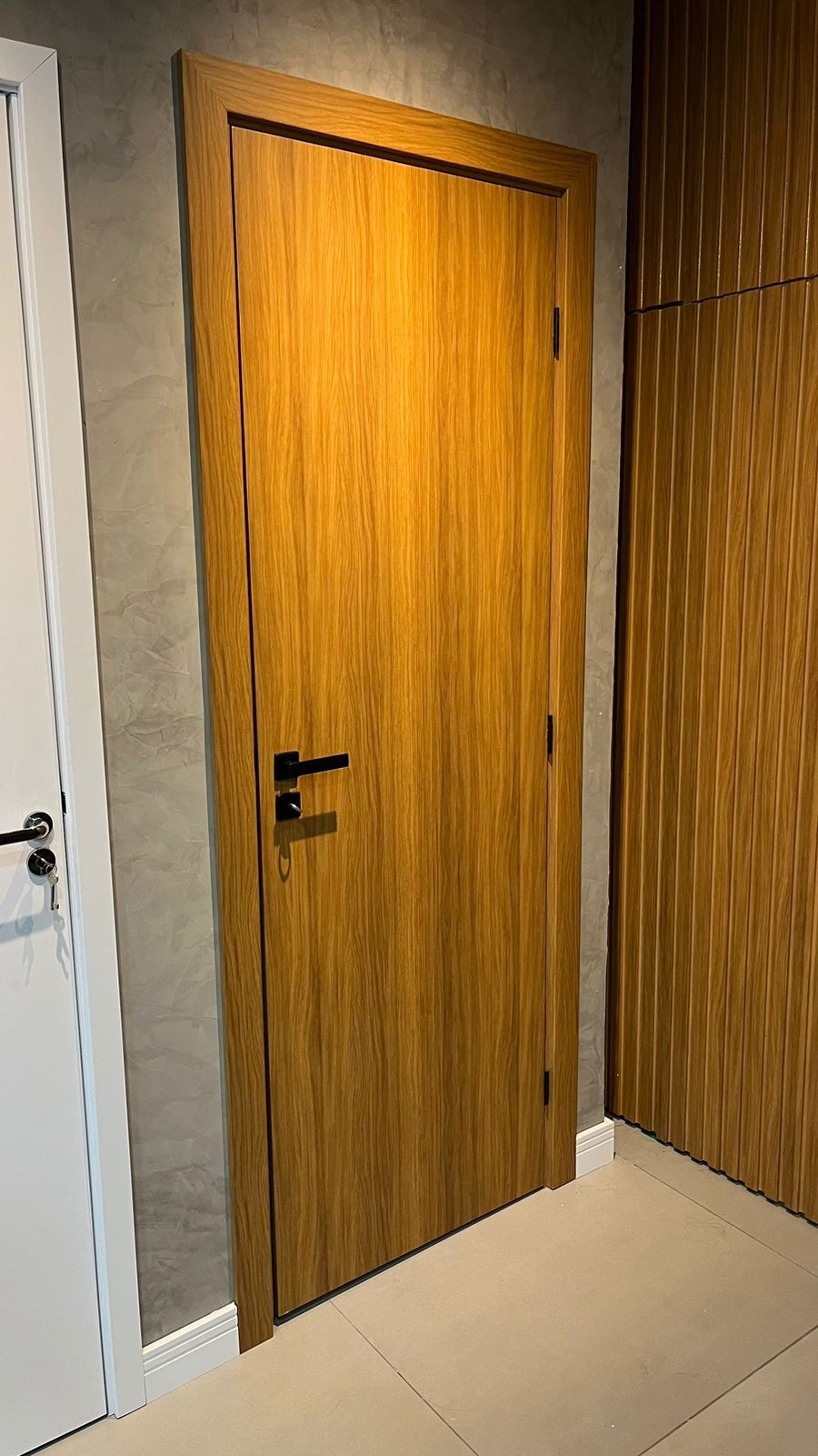 Uma porta de madeira está em um corredor ao lado de uma porta branca.