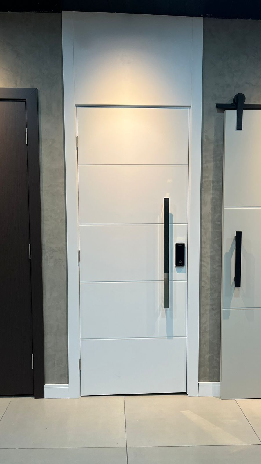 Uma porta branca com uma maçaneta preta está ao lado de uma porta preta.