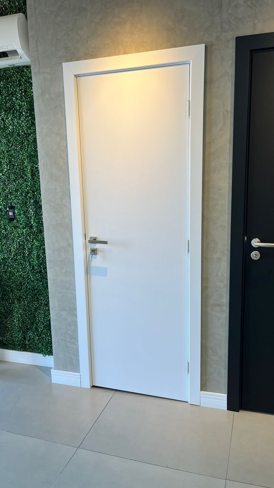 Uma porta branca está em um corredor ao lado de uma porta preta.