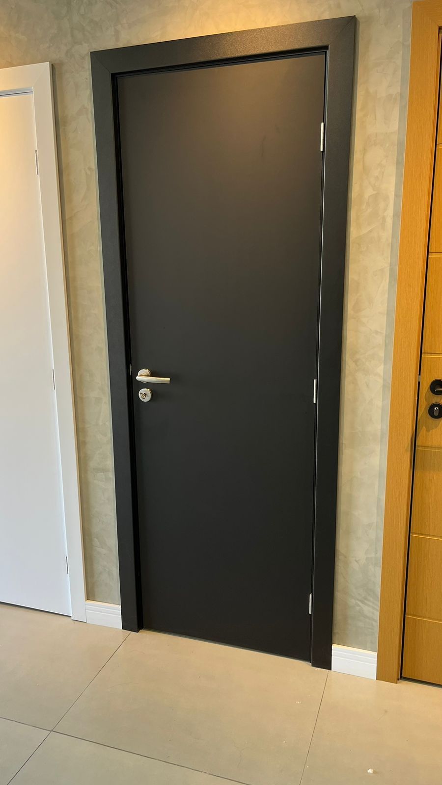 Uma porta preta está em um corredor ao lado de uma porta branca.