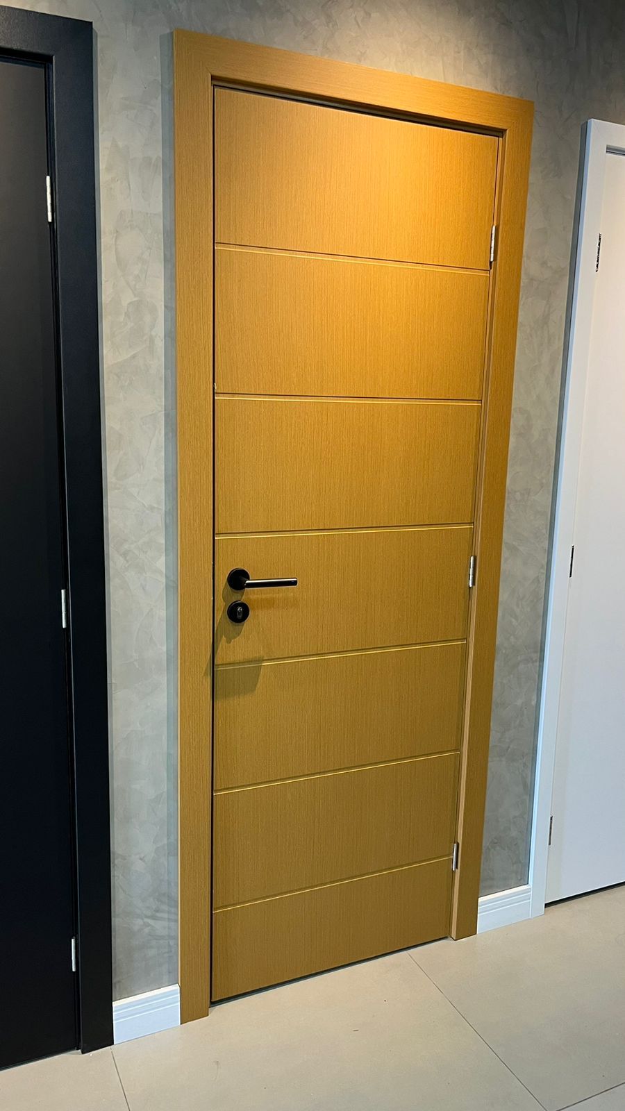 Uma porta de madeira está em um corredor ao lado de uma porta preta.