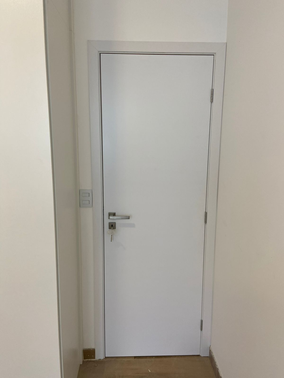 Uma porta branca está em um corredor ao lado de uma parede branca.