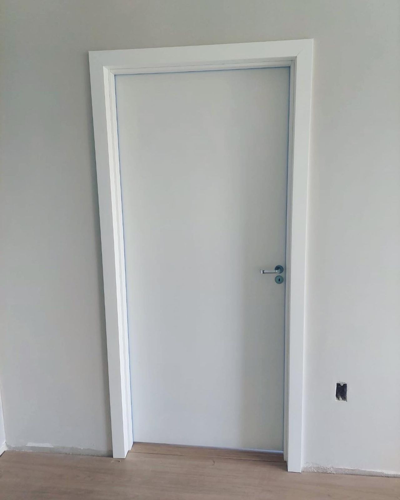 Uma porta branca está em uma sala com piso de madeira.