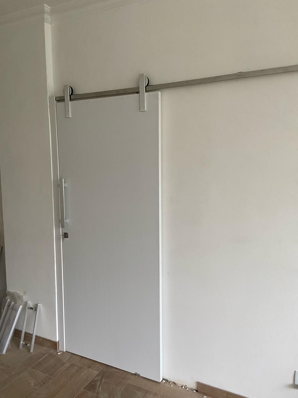 Uma porta de celeiro branca de correr está pendurada em uma parede branca em uma sala.