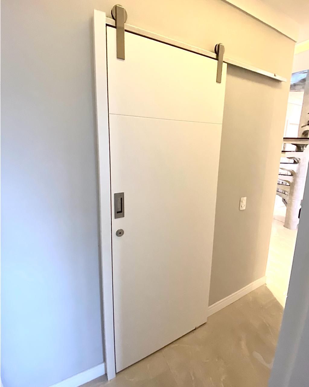 Uma porta de celeiro branca de correr está pendurada na parede de um corredor.