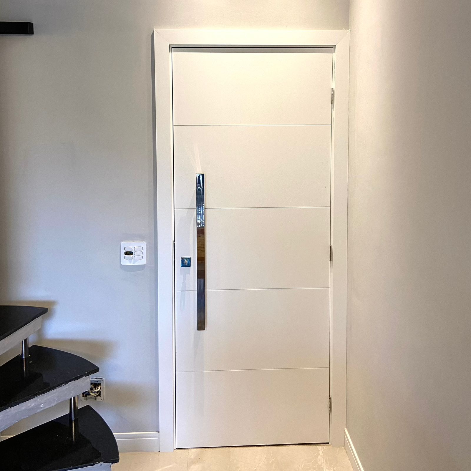 Uma porta branca com uma maçaneta de aço inoxidável fica em um corredor.