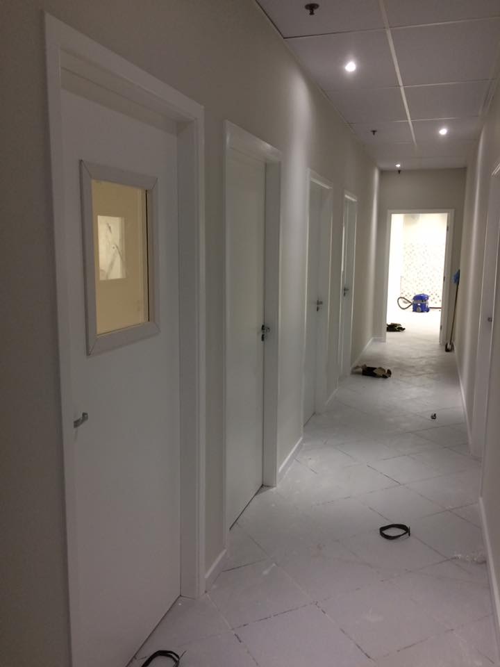 Um longo corredor com portas brancas e uma janela.