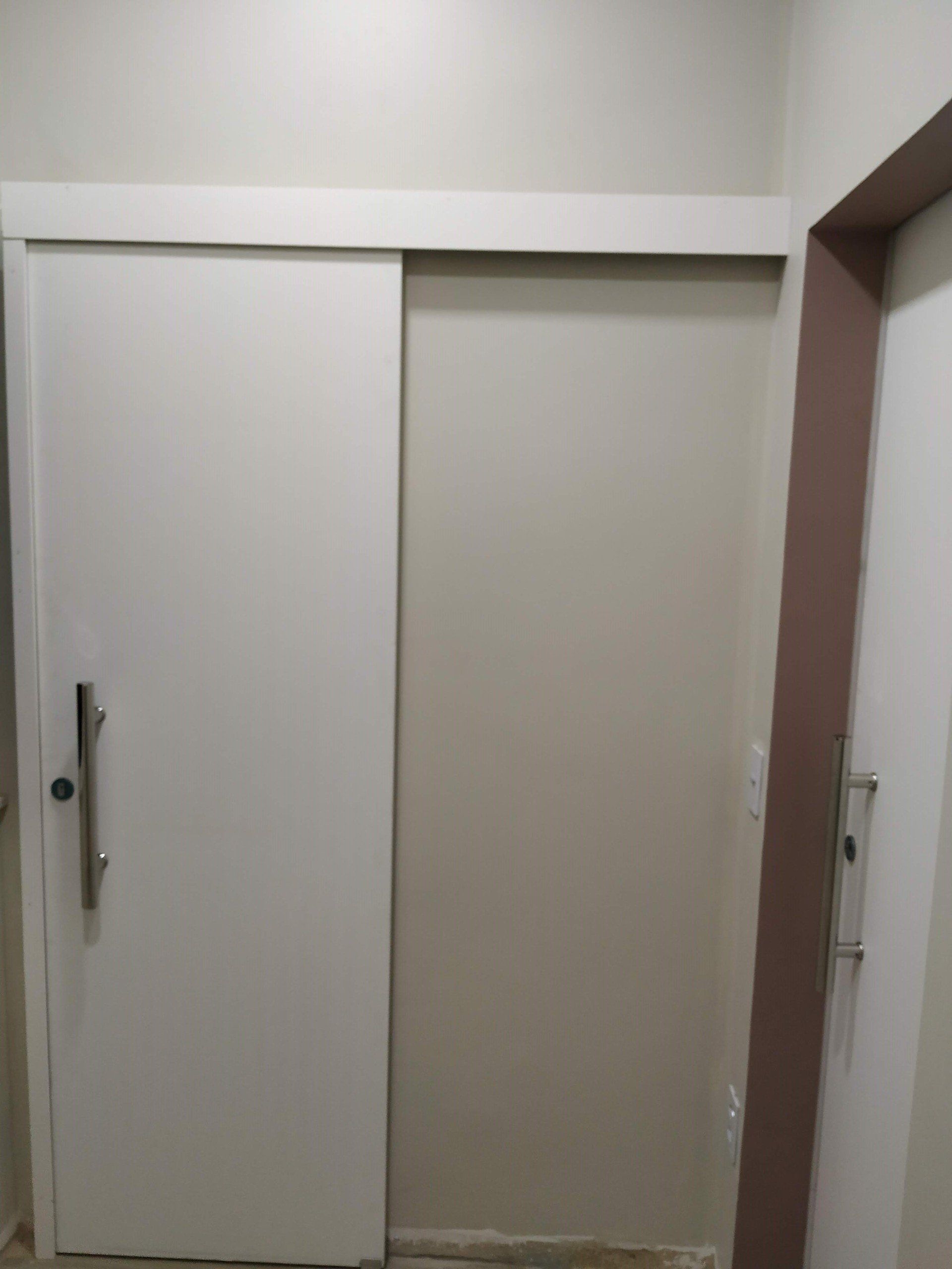 Uma porta de correr branca com uma maçaneta em um corredor.