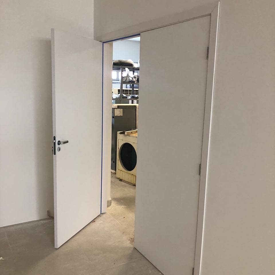 Uma porta branca está aberta para uma sala com uma máquina de lavar e secar roupa.