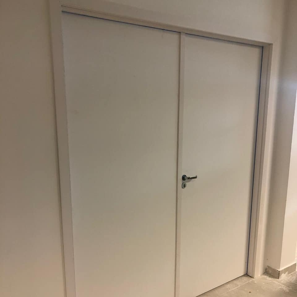 Um par de portas brancas com uma maçaneta em um corredor.