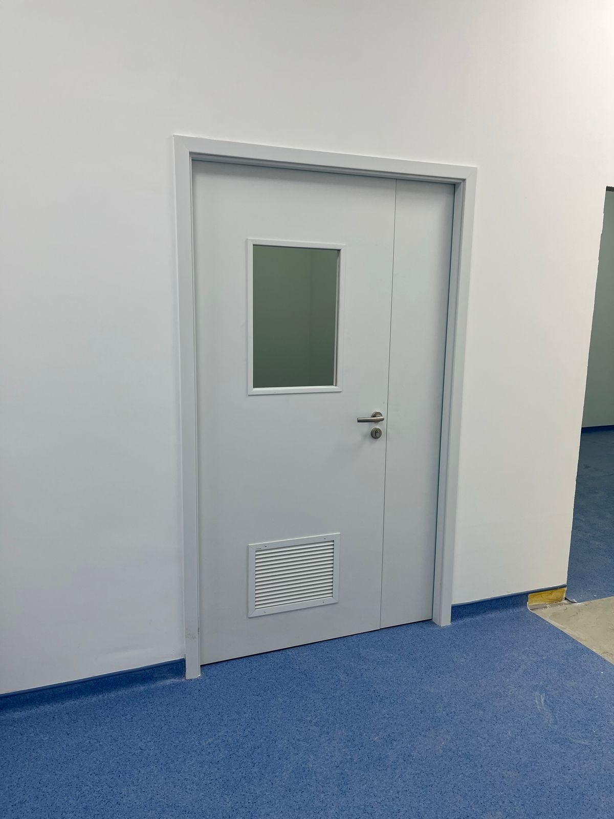 Uma porta branca com uma pequena janela em um corredor.