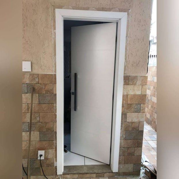 Uma porta branca está aberta em uma sala com uma parede de tijolos.