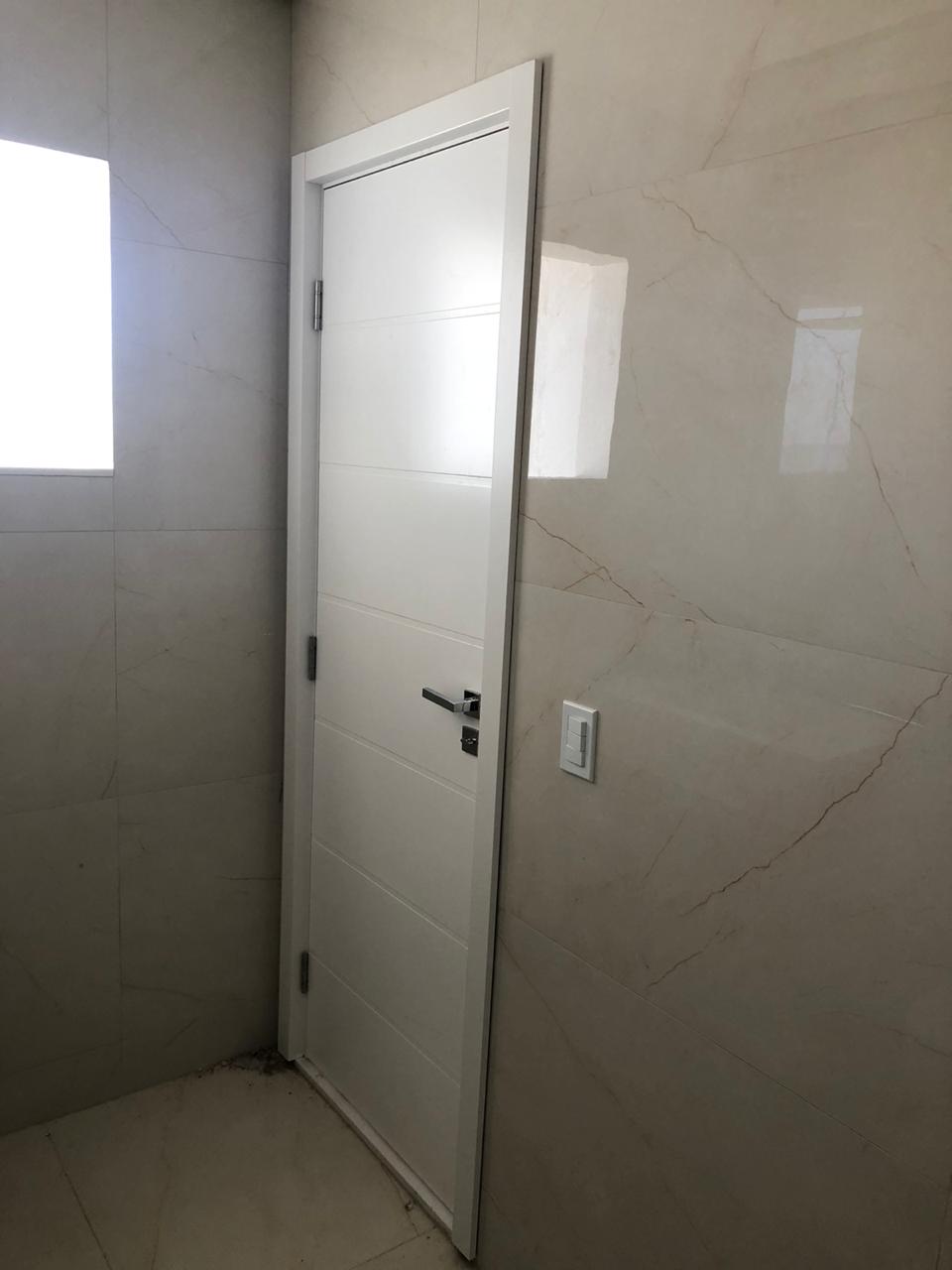 Uma porta branca está em um banheiro ao lado de uma janela.