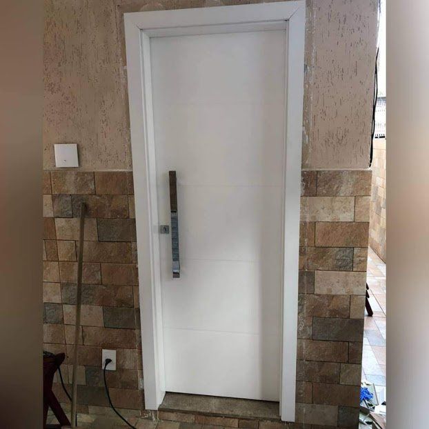 Uma porta branca está em uma sala com uma parede de tijolos.