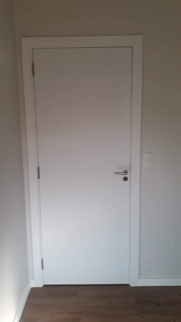 Uma porta branca está em uma sala com piso de madeira.