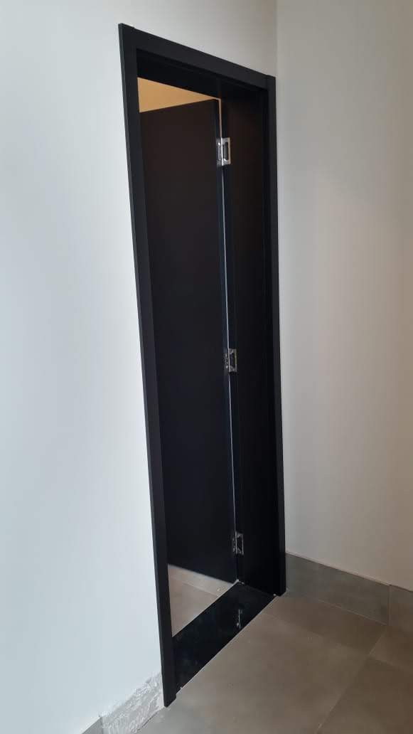 Uma porta preta está aberta em um corredor com uma parede branca.