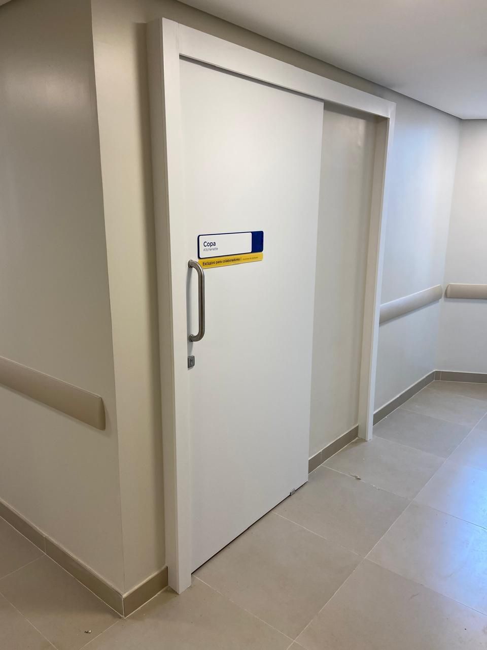 Uma porta de correr branca está em um corredor de hospital.