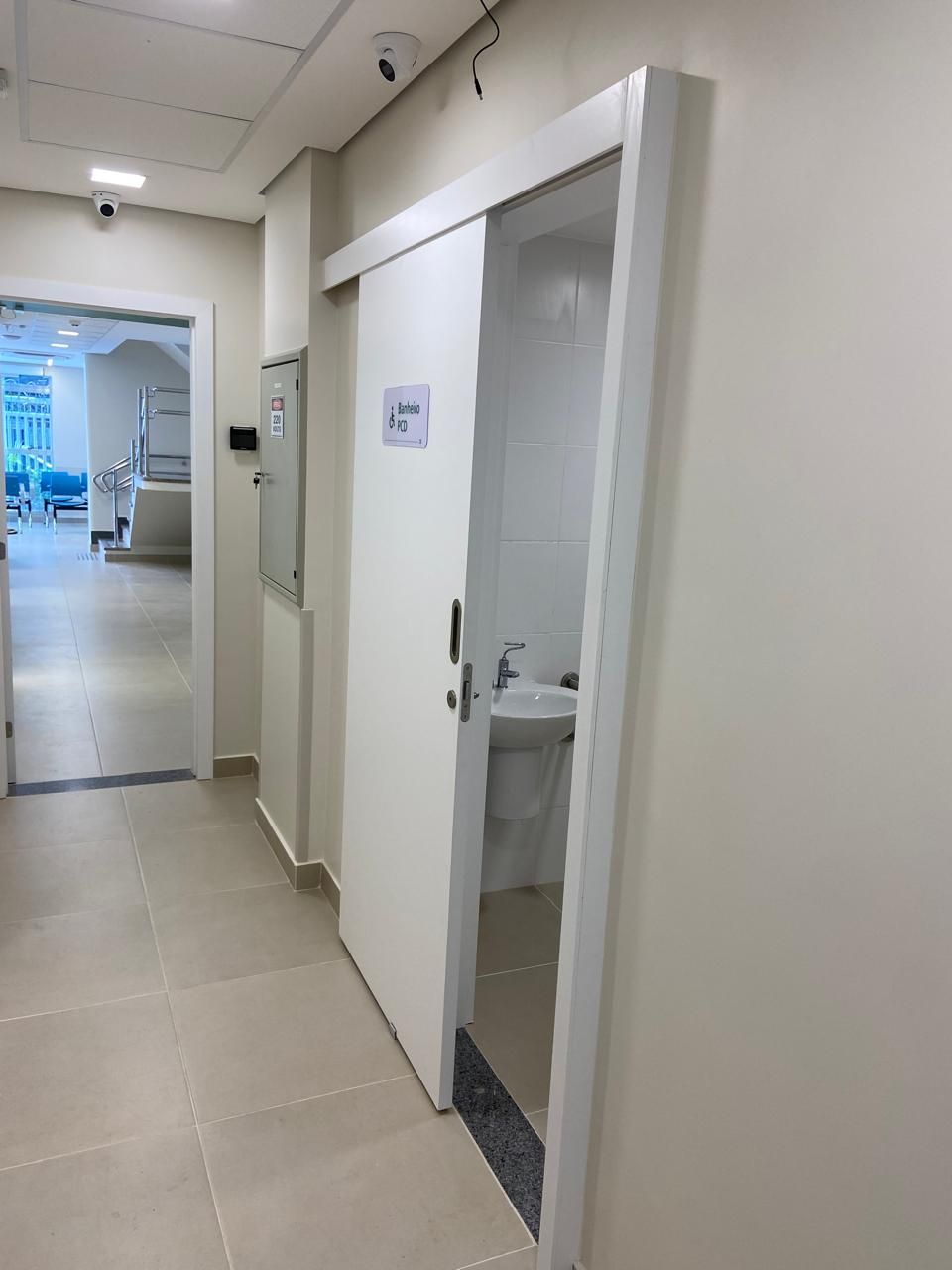 Um corredor de hospital com uma porta de correr que leva a um banheiro