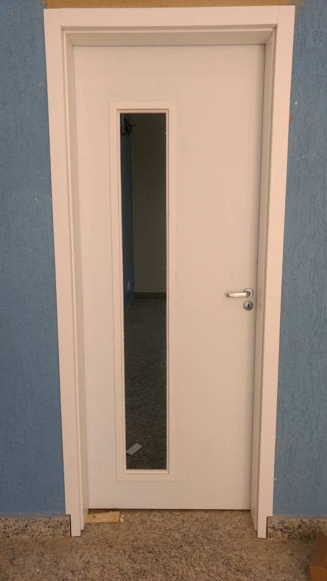 Uma porta branca com uma pequena janela está contra uma parede azul.
