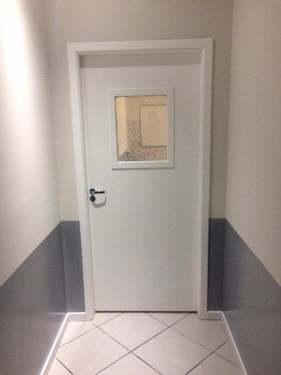 Uma porta branca com uma pequena janela em um corredor