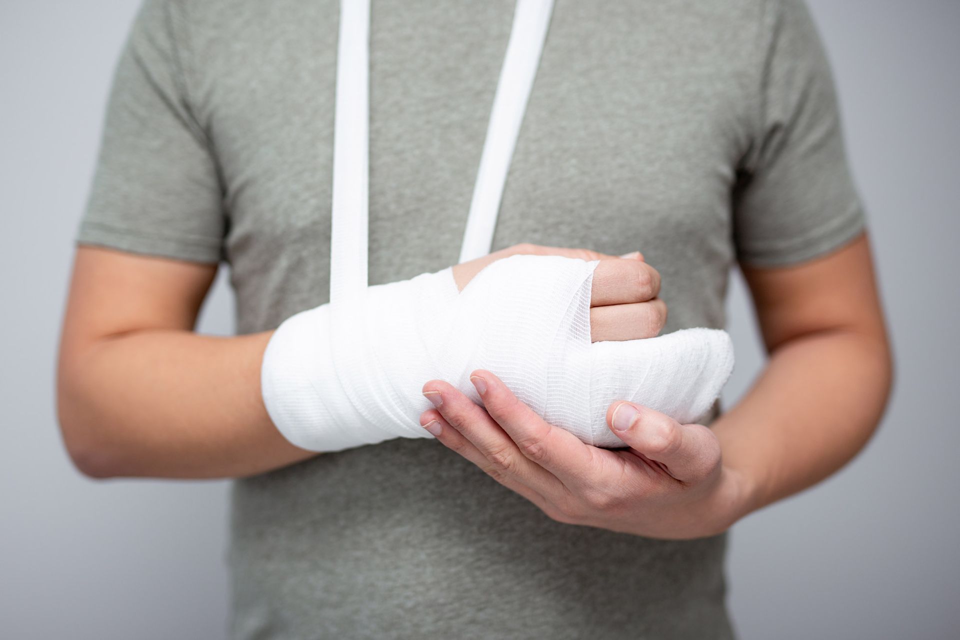 Person holding arm in a white cast, supported by a sling, against a gray background.