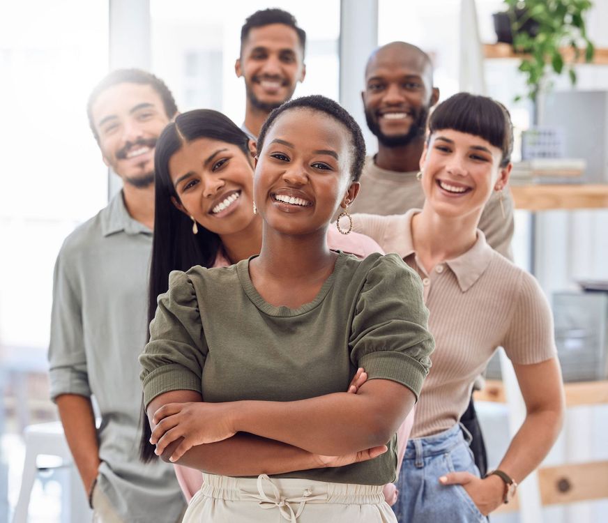 A diverse group of smiling professionals standing together in an office, with a woman in the center posing with arms crossed.