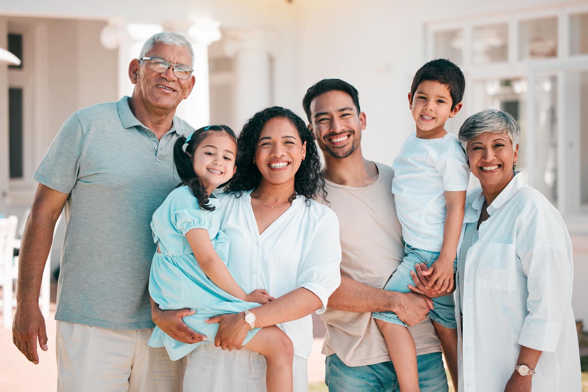 Family of six smiling together outdoors in front of a white building.