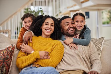 Family of four smiles together on a couch; two children hug their parents.