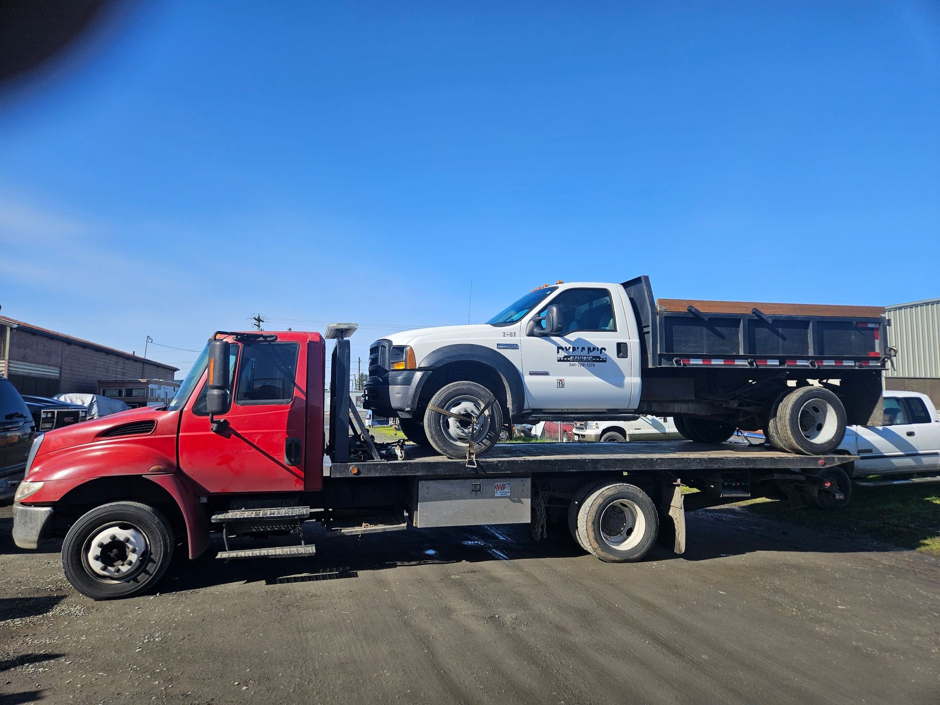 A red tow truck is carrying a white truck on the back of it.