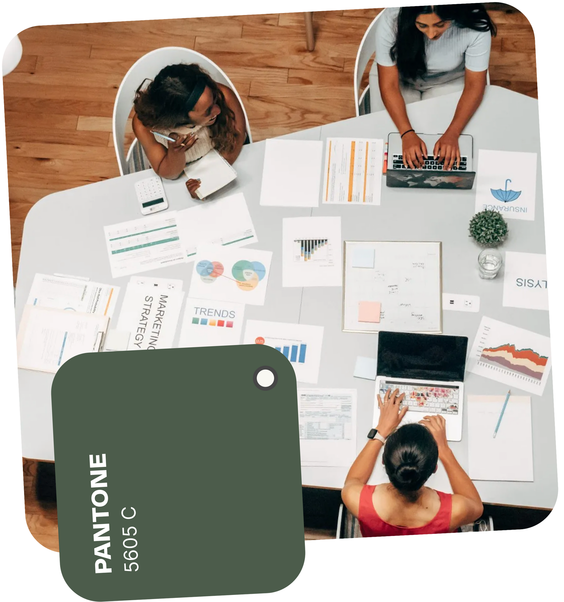 People working collaboratively at a table with papers, laptops, and a Pantone 5605 C color swatch.
