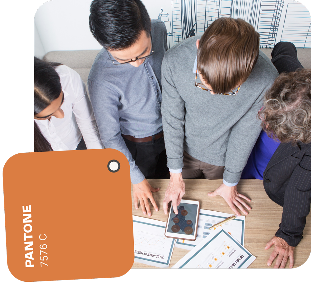 People gathered around a table with papers and a tablet. A Pantone color swatch of orange is in the image.