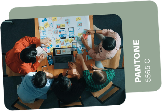 Team of people collaborating around a table, brainstorming designs. Pantone color 5565 C.