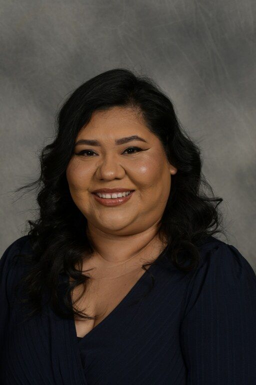 Portrait of a smiling woman in a dark blue top against a gray studio backdrop