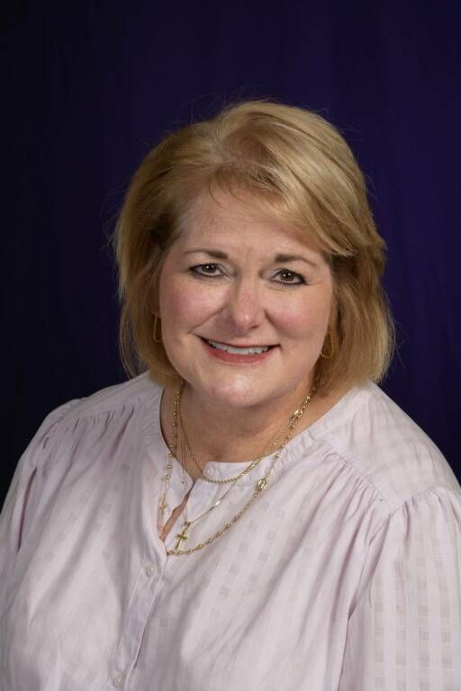 Smiling woman in a light blouse and necklace against a dark purple backdrop