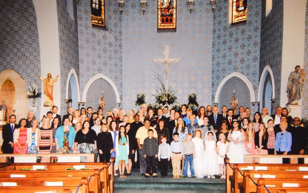 Large group posing inside a church sanctuary with a cross, altar, and stained-glass windows.