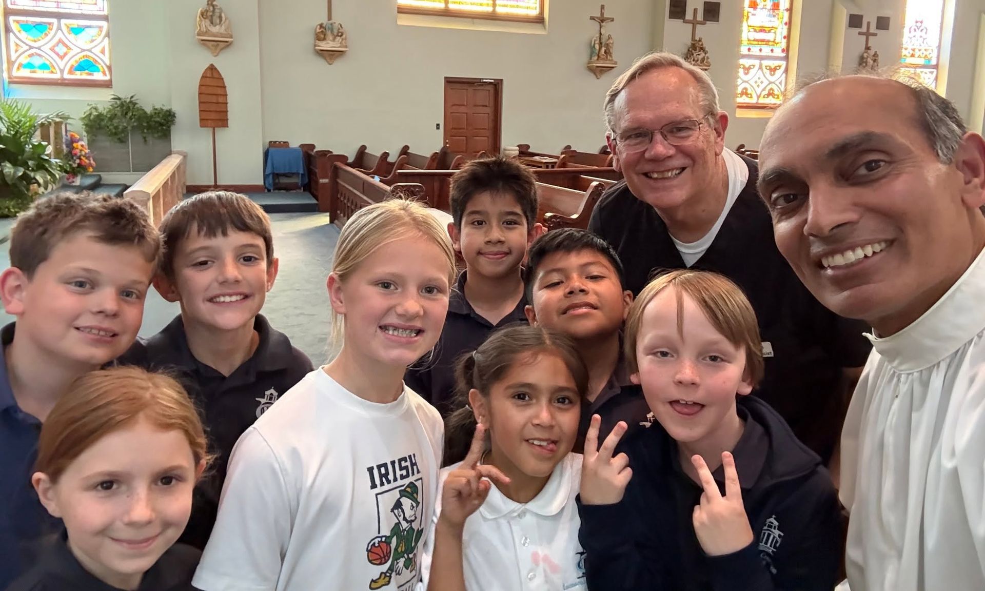 Group posing in a church with a priest, standing before an altar and cross.